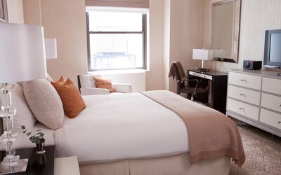 Double bed guest room in The Benjamin Royal Sonesta New York, furnished with TV, armchair, and workspace desk and chair.