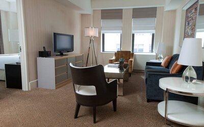 The Benjamin Royal Sonesta New York guest room, featuring chairs, sofa, coffee table, windows, and a television.