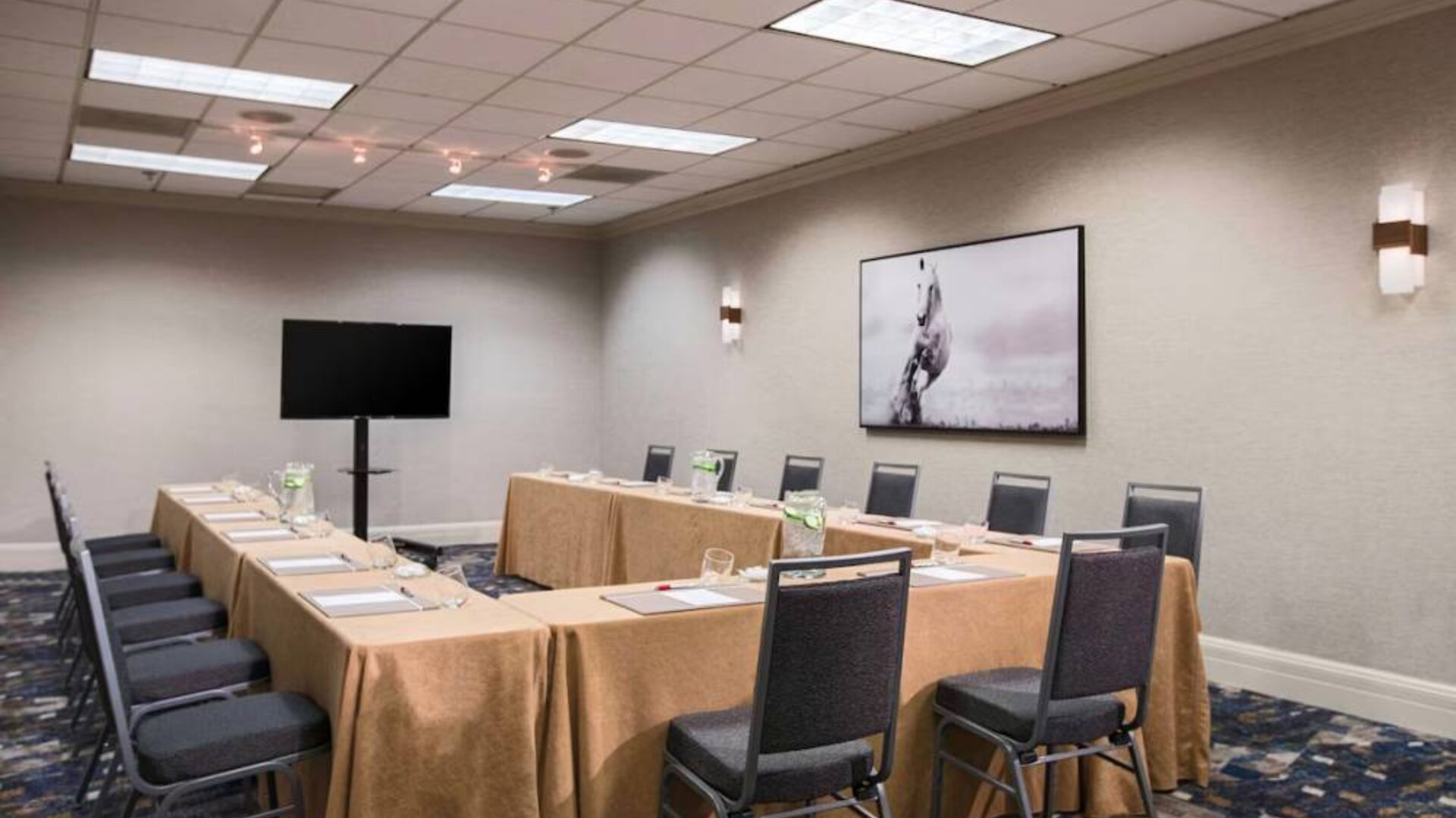 Meeting room in with tables arranged in a U-shape facing  large TV, plus a large artistic photograph of a horse on the wall.