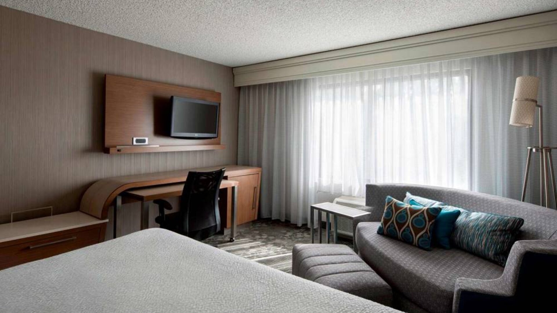 Sonesta Select Tempe Downtown double bed guest room, furnished with TV and sofa, plus workspace desk and chair.