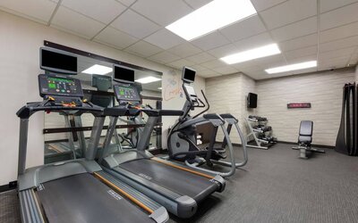 The fitness center in Sonesta Select Tempe Downtown has a wall-mounted TV, free weights, and exercise machines facing a large mirror.