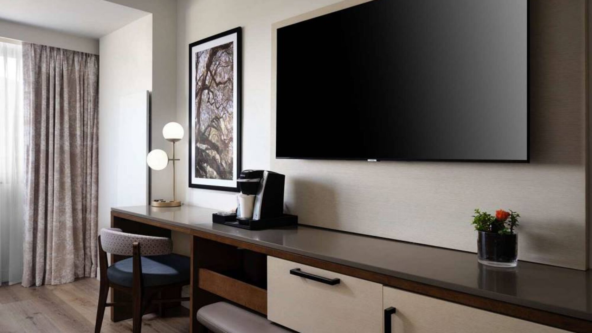 Sonesta Irvine guest room workspace, furnished with desk, chair, and lamp, plus a nearby widescreen TV.
