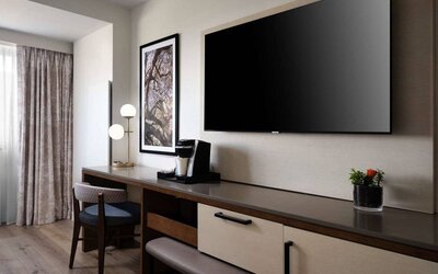 Sonesta Irvine guest room workspace, furnished with desk, chair, and lamp, plus a nearby widescreen TV.