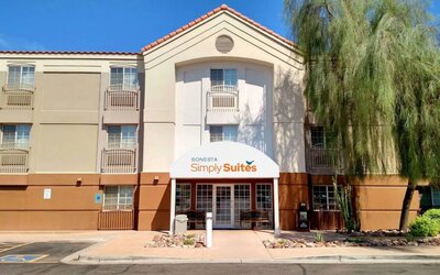 The hotel’s exterior has a pair of benches beneath the covered entranceway, disabled parking spaces nearby, and a towering tree.