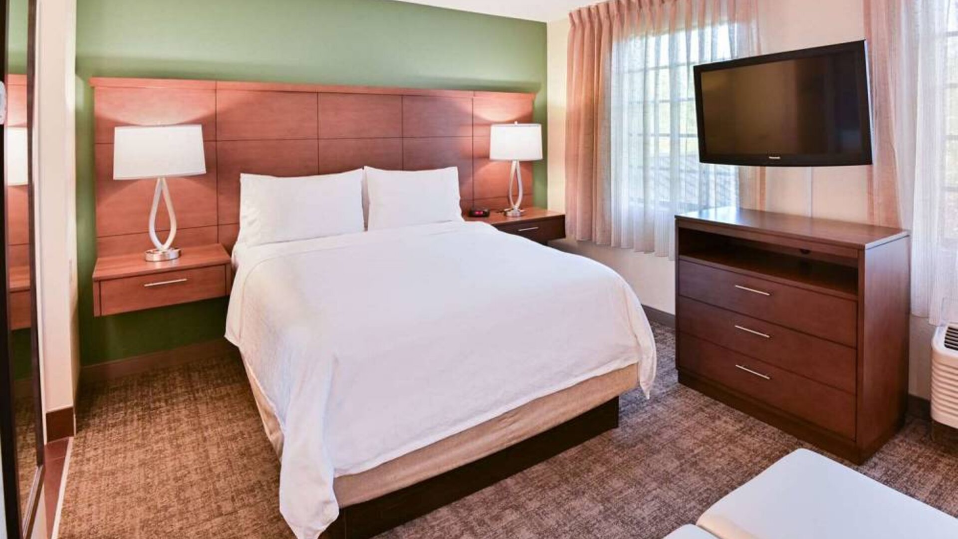 Double bed guest room in Sonesta ES Suites Fort Lauderdale Plantation, featuring bedside lamps, windows, and a large TV.