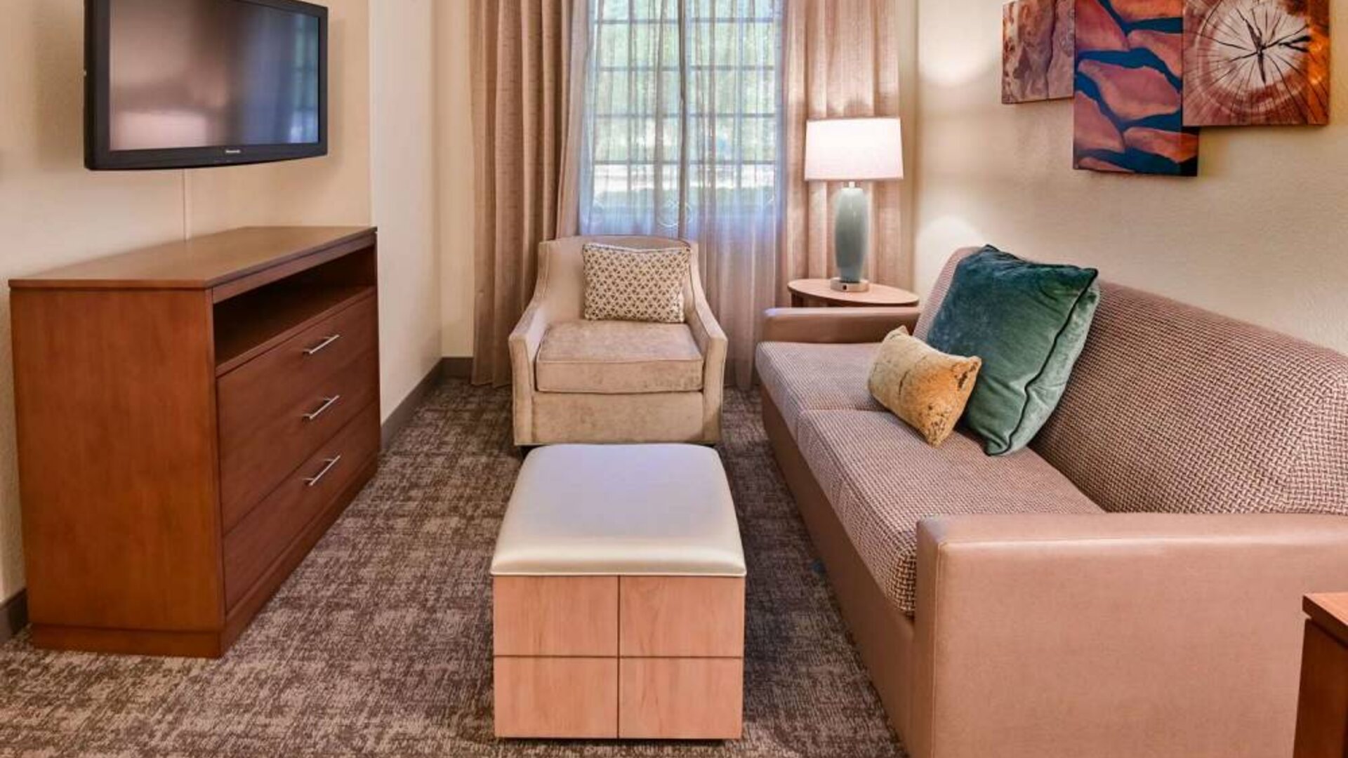 Sonesta ES Suites Fort Lauderdale Plantation guest room living area, furnished with sofa, armchair, window, and a widescreen television.