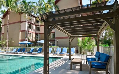Sonesta ES Suites Fort Lauderdale Plantation’s outdoor pool has sofa seating and a coffee table by the side, alongside a row of sun loungers.