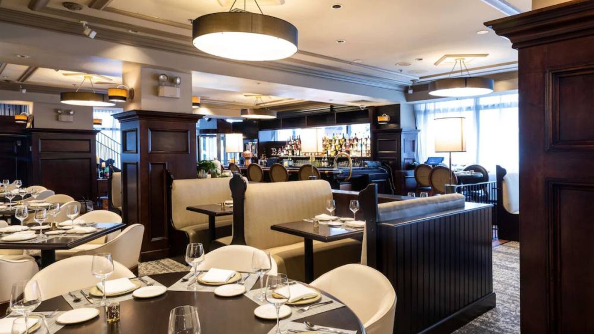 The hotel’s restaurant offers both table and booth seating, with a mix of white seats and dark wood tables, plus a bar.