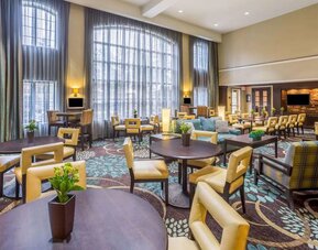 The hotel’s breakfast area has a carpeted floor, range of table sizes, seating from normal chairs to tall stools and armchairs, high ceilings and large windows, plus multiple TVs.