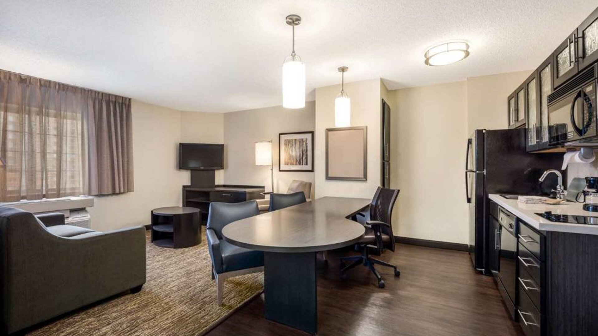 Sonesta Simply Suites Parsippany Morris Plains guest room living area, furnished with table and chairs, sofa, window, and TV.