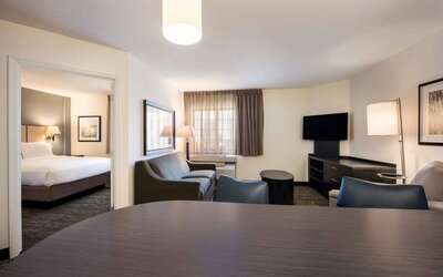 Double bed guest room in Sonesta Simply Suites Oklahoma City Airport, including a living area with sofa, TV, window, and a table and chairs.