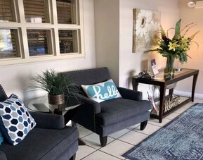 The hotel lobby is furnished with a pair of armchairs, a coffee table, art on the wall, and potted plants.