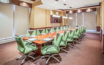 Hotel meeting room, furnished with a long wooden table and 18 green swivel chairs.