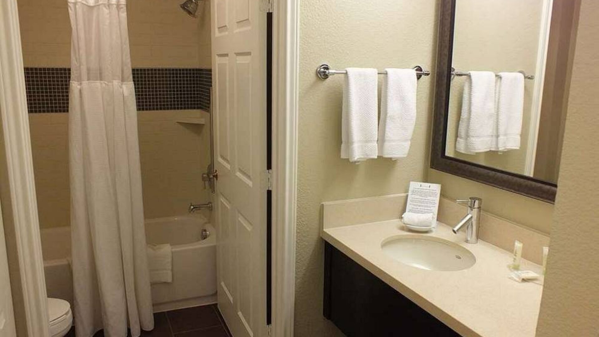 Guest bathroom in Sonesta ES Suites Dallas Las Colinas, featuring bath with a shower, lavatory, and mirror and sink.