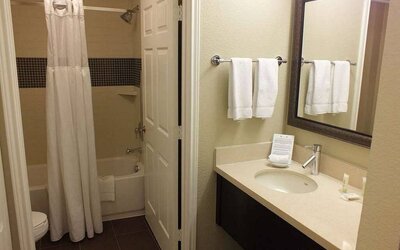 Guest bathroom in Sonesta ES Suites Dallas Las Colinas, featuring bath with a shower, lavatory, and mirror and sink.