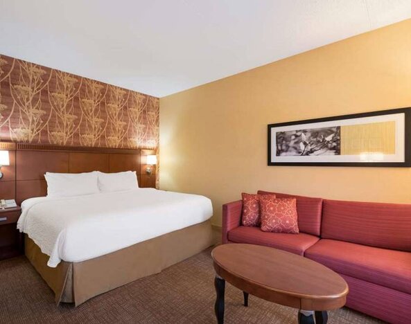 Sonesta Select Detroit Auburn Hills double bed guest room, furnished with art on the wall, a coffee table, and a red sofa with cushions.