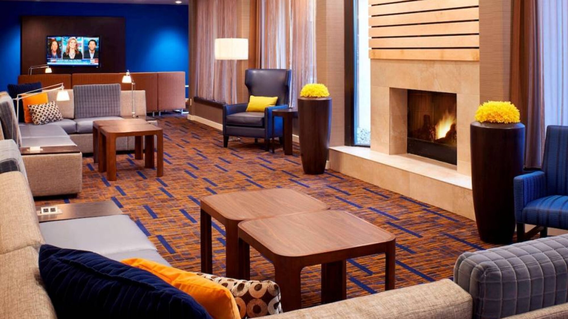 Sonesta Select Detroit Auburn Hills’ lobby lounge is furnished with sofas, armchairs, coffee tables, a fireplace and a wall-mounted TV.