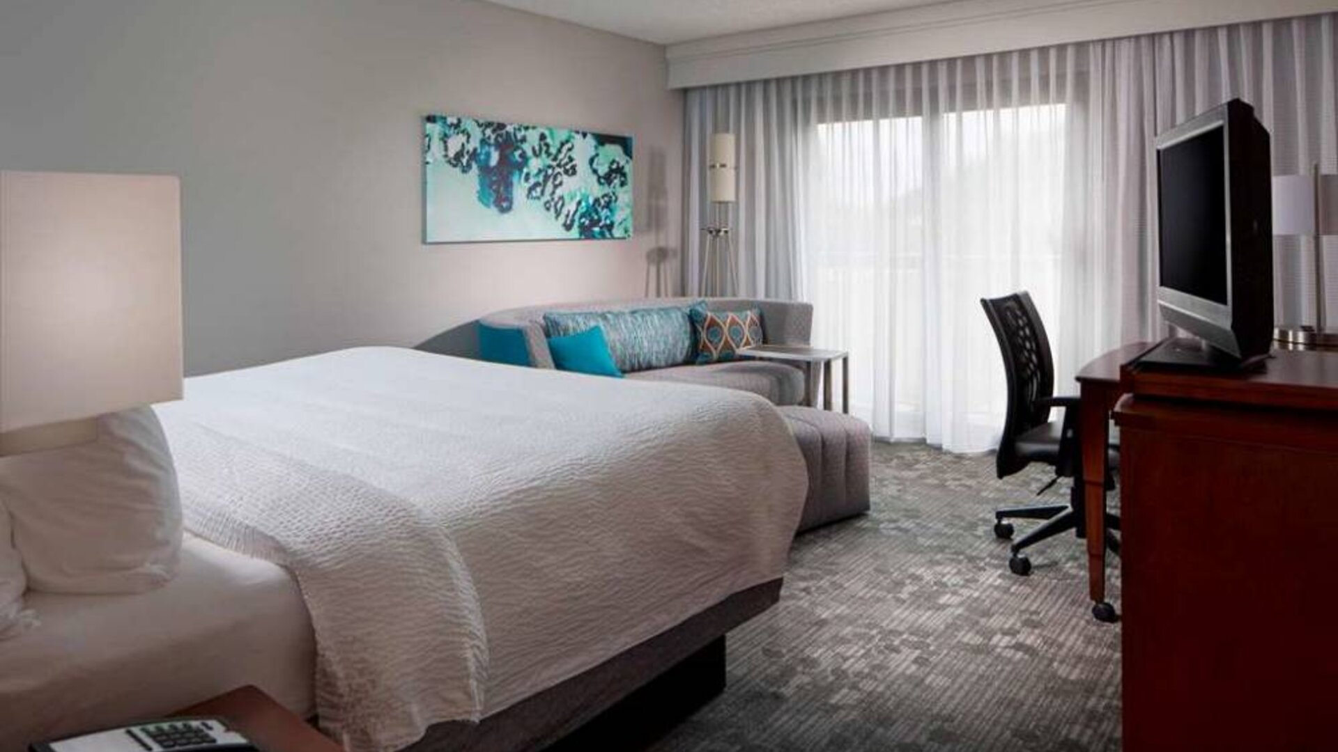 Sonesta Select Boca Raton double bed guest room, including sofa, window, TV, and a workspace desk and chair.