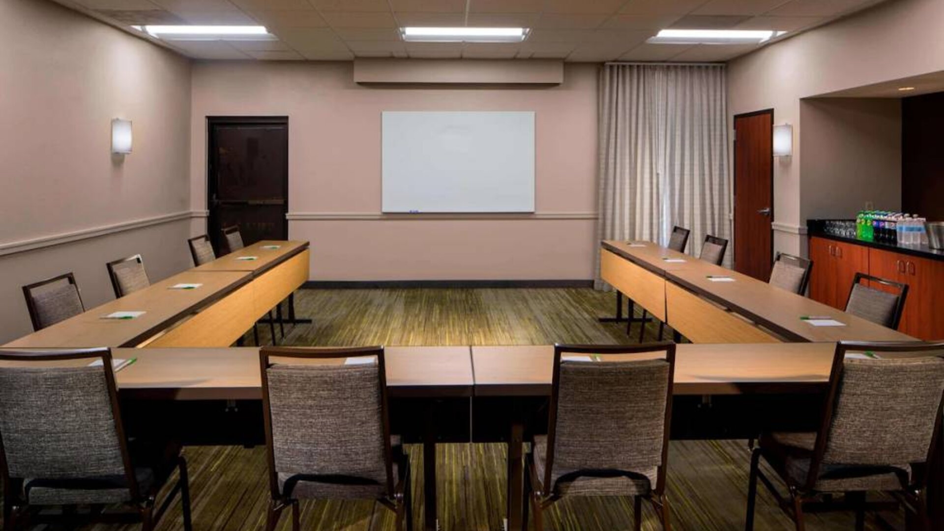 Hotel meeting room, featuring tables arranged in a U-shape, seating for a dozen attendees, and a whiteboard.
