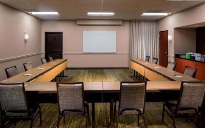 Hotel meeting room, featuring tables arranged in a U-shape, seating for a dozen attendees, and a whiteboard.