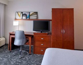 Sonesta Select Indianapolis Carmel guest room workspace, furnished with bed and TV, plus desk, chair, and lamp.