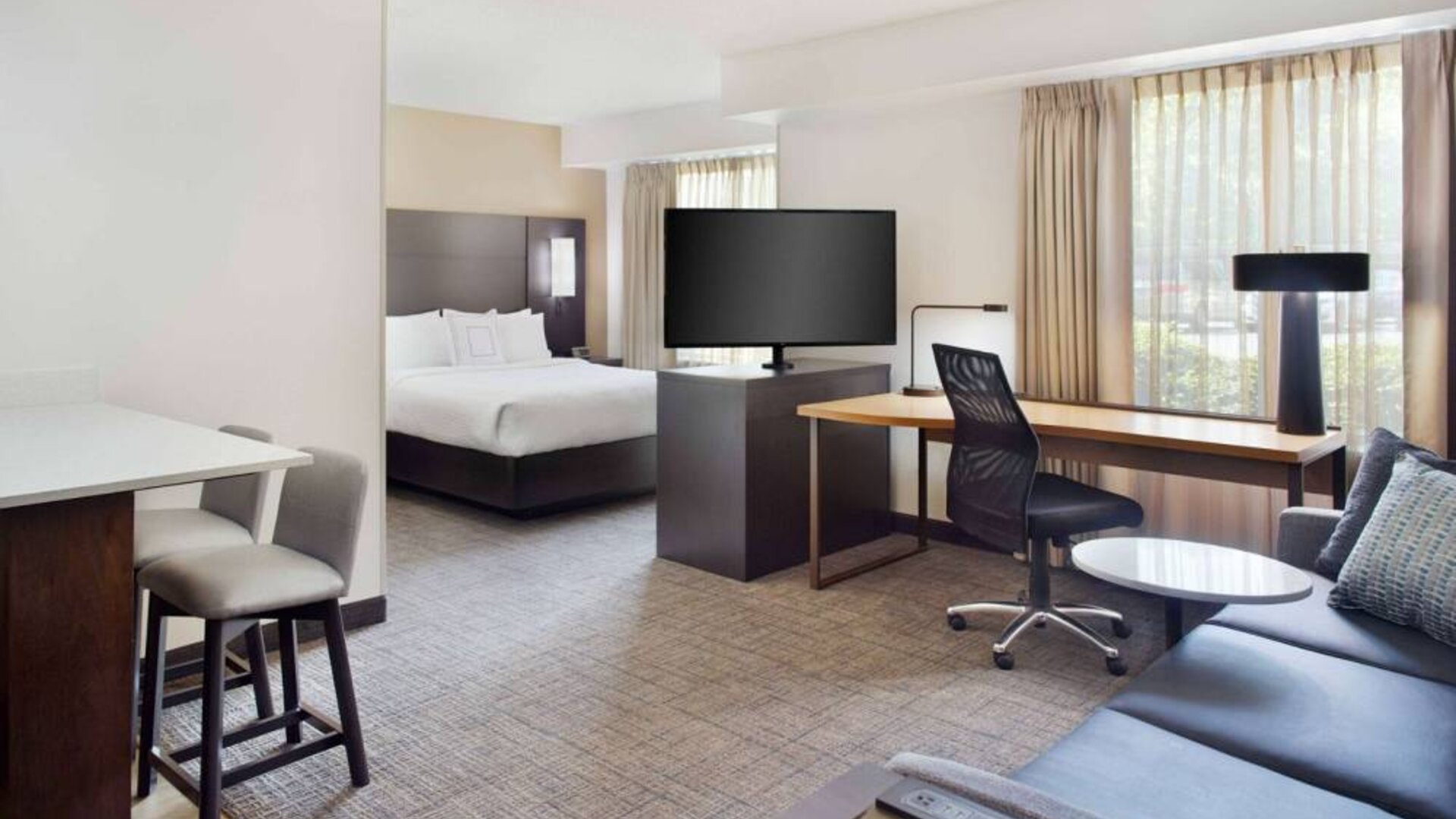 Double bed guest room in Sonesta ES Suites Raleigh Cary, featuring TV and sofa, plus workspace desk, chair, and lamp.