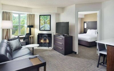 Sonesta ES Suites Raleigh Cary double bed guest room, with a living area furnished with sofa, coffee table, fireplace, and TV.