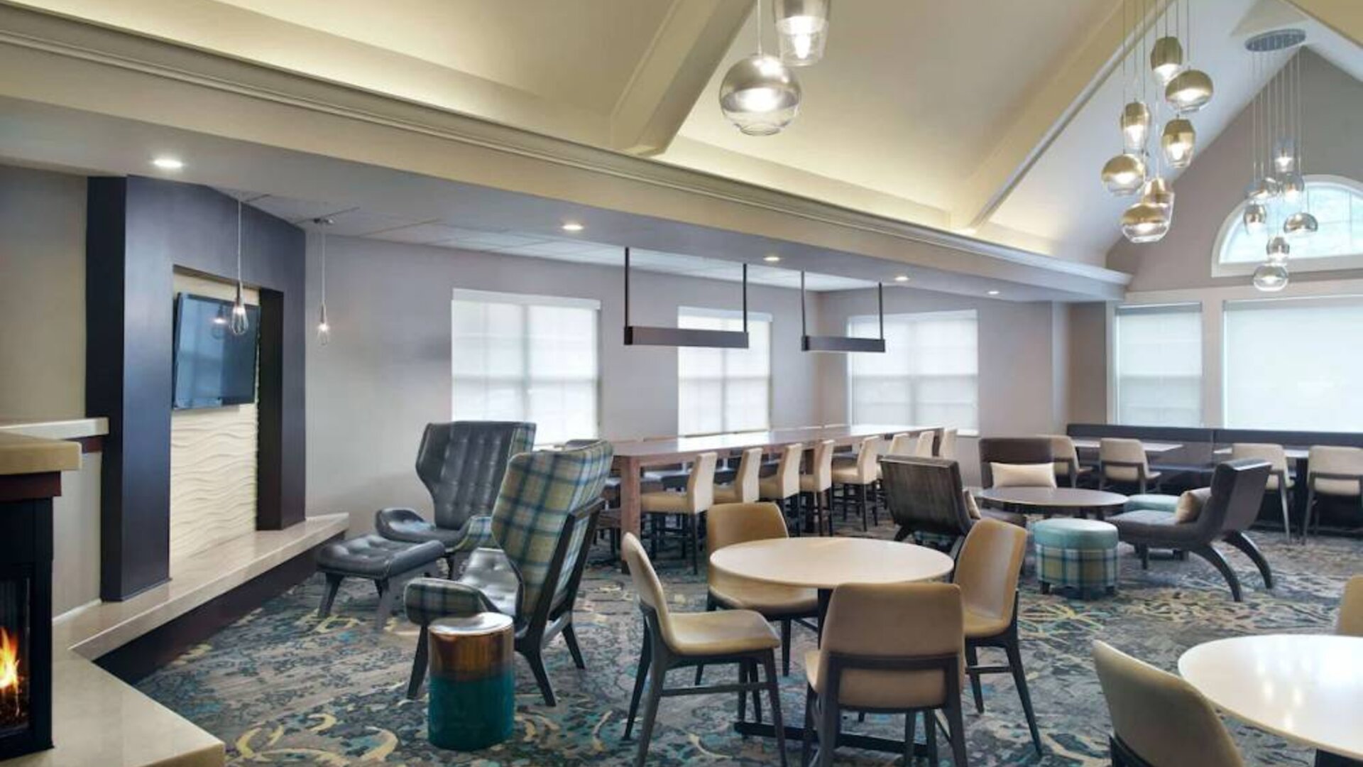 Sonesta ES Suites Raleigh Cary’s lobby has extensive seating and range of table sizes, plus large windows, TV, and a fireplace.
