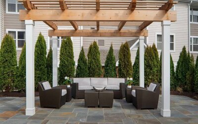 Sonesta ES Suites Fairfax Fair Lakes’s patio is furnished with armchair and sofa seating, plus coffee tables and nearby greenery.