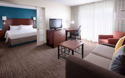 Double bed guest room in Sonesta ES Suites Dallas Medical Market Center, featuring a living area with sofa, armchair, and TV.