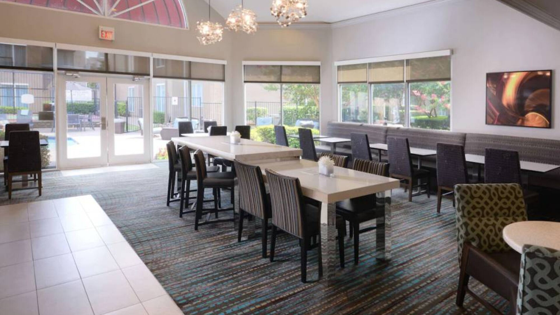 Sonesta ES Suites Dallas Medical Market Center’s lobby is furnished with a mix of table sizes and both regular and tall chairs, with plenty of natural light flowing through large windows.