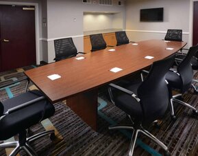 Hotel meeting room, with long wooden table, eight swivel chairs, and a wall-mounted television.