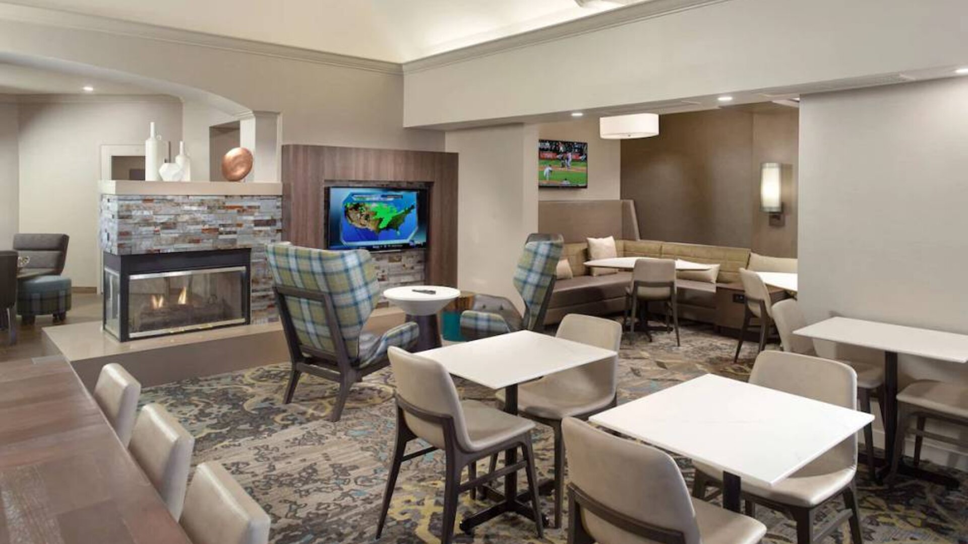Lobby lounge furnished with sofa seating, tables and chairs, a fireplace and TV, at Sonesta ES Suites Raleigh Durham Airport Morrisville.