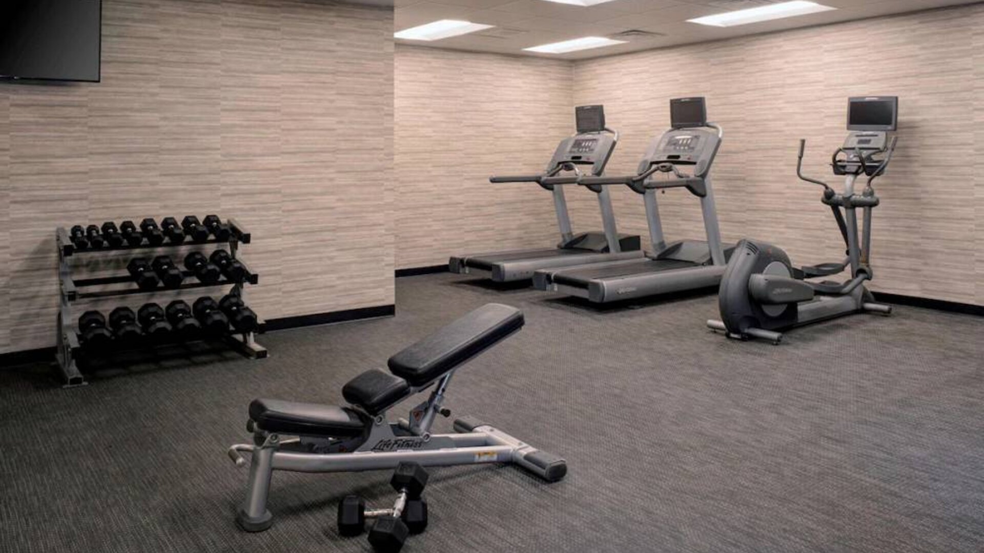 Fitness center furnished with free weights, assorted exercise machines, and a TV at Sonesta Select Kansas City South Overland Park.