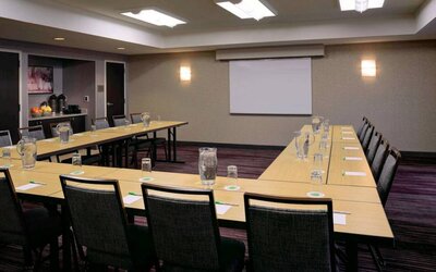 Hotel meeting room with a projector screen and tables arranged in a U-shape.