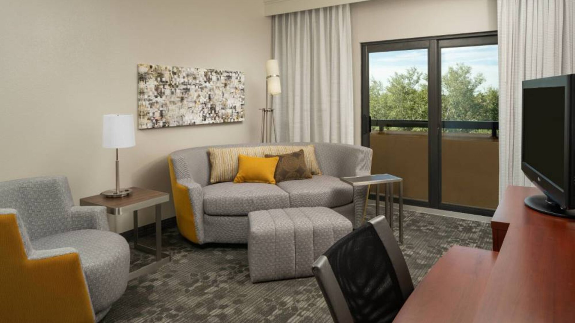 Guest room living area in Sonesta Select Miami Lakes, including sofa, chair, and TV.