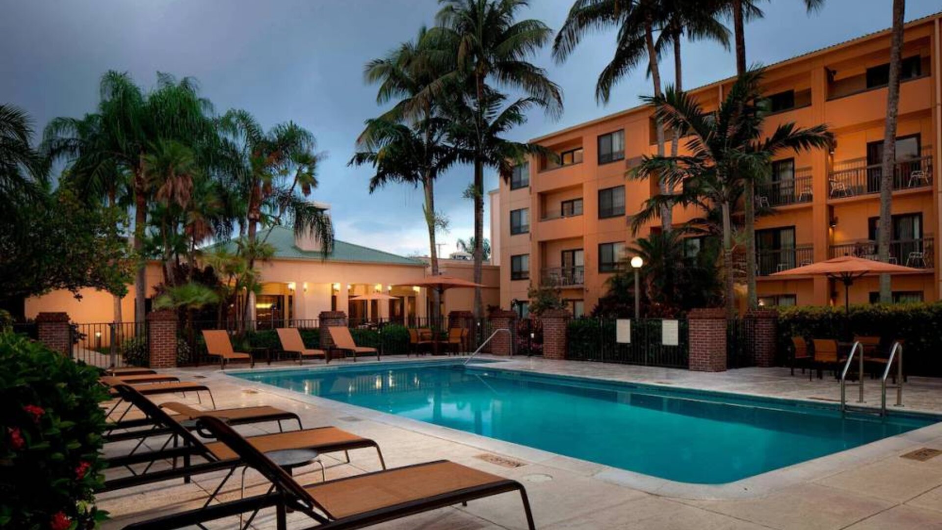 Outdoor pool a mix of sun loungers and shaded tables and chairs by the side, at Sonesta Select Miami Lakes.