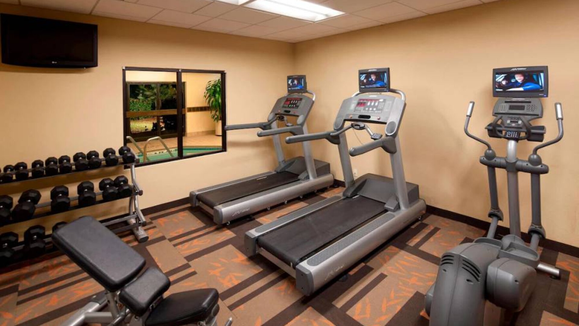 Sonesta Select Miami Lakes’ fitness center is equipped with various exercise machines, free weights, and a wall-mounted TV.