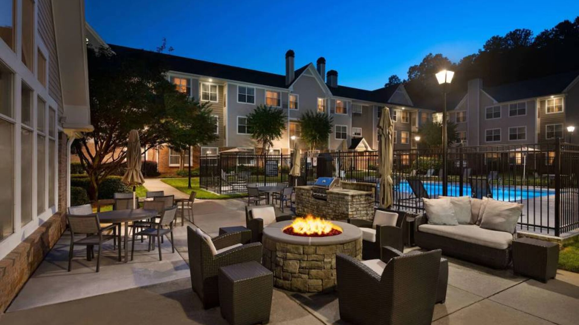 Patio area with fire pit, barbecue, tables and chairs, and armchairs, at Sonesta ES Suites Atlanta Alpharetta North Point Mall.
