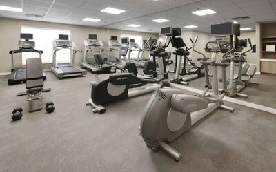 Fitness center at Sonesta ES Suites Fort Worth Fossil Creek, featuring free weights, a mirrored wall, and range of exercise machines.