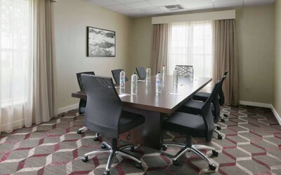 Meeting room in Sonesta ES Suites Fort Worth Fossil Creek, furnished with long wooden table and eight swivel chairs.