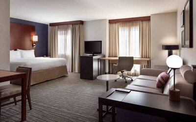 Double bed guest room living area in Sonesta ES Suites Tempe, furnished with sofa, coffee table, chair, desk, and TV.