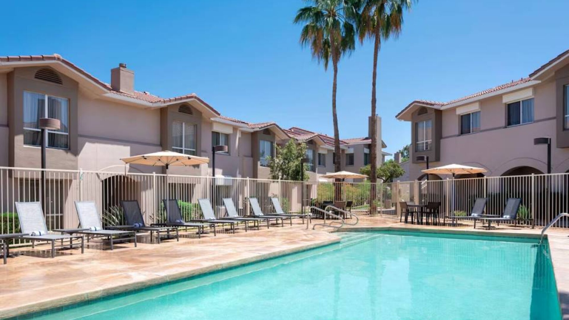 Outdoor pool at Sonesta ES Suites Tempe, featuring shaded tables and chairs, plus sun loungers, by the side.