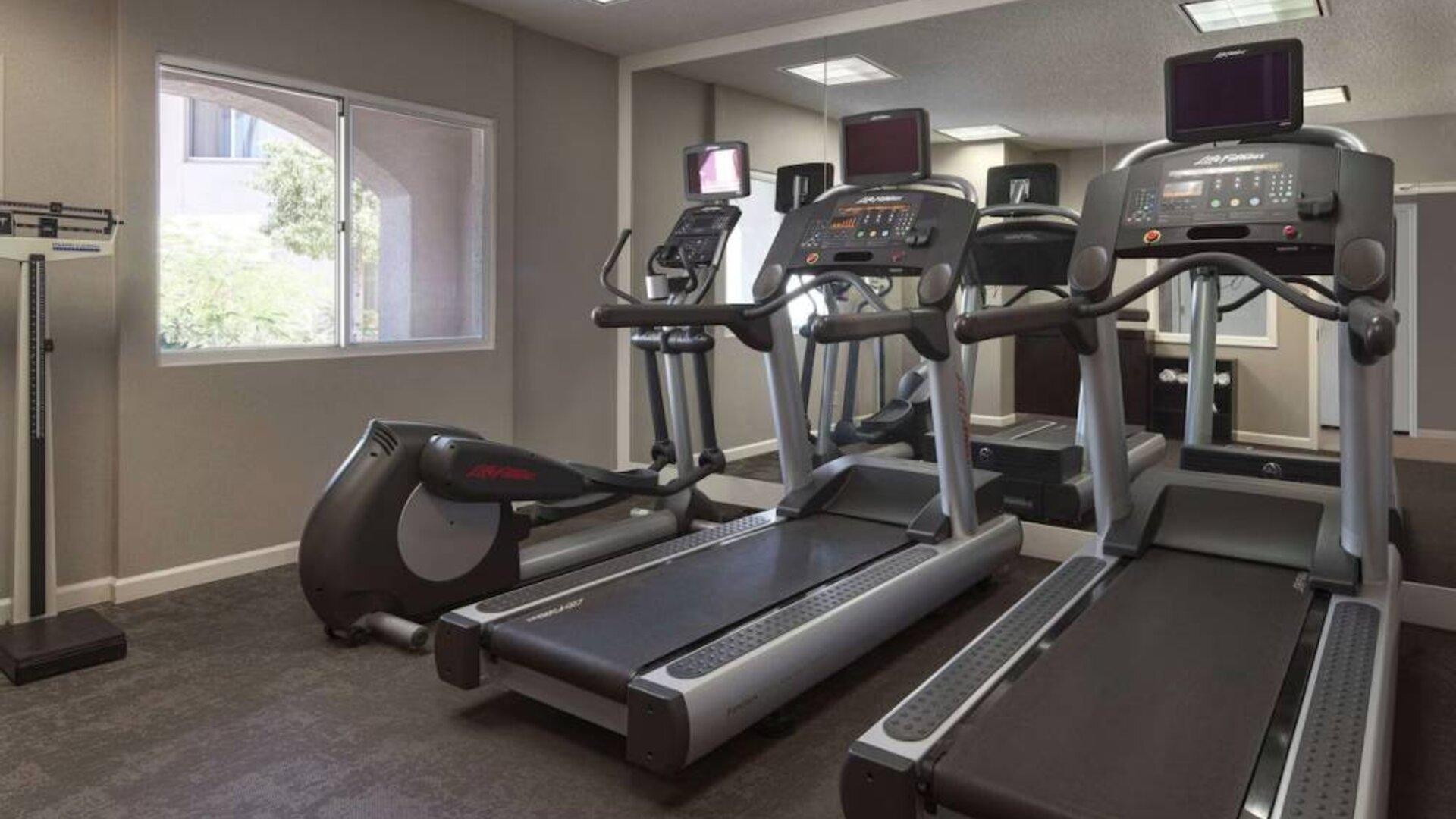 Sonesta ES Suites Tempe’s fitness center has a window, mirrored wall, treadmills, and an elliptical machine.