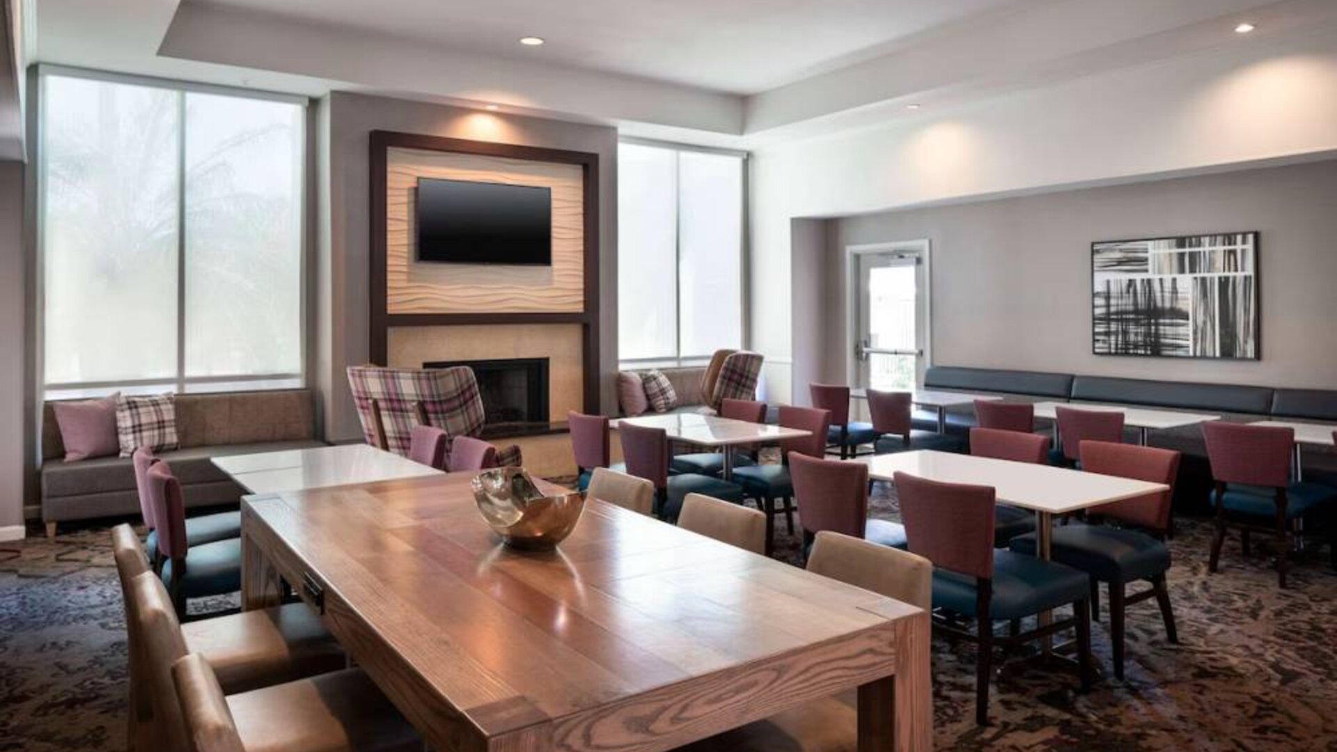 Breakfast area in Sonesta ES Suites Tempe, with mix of table sizes, sofas and chairs, large windows, and a wall-mounted television.