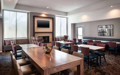 Breakfast area in Sonesta ES Suites Tempe, with mix of table sizes, sofas and chairs, large windows, and a wall-mounted television.