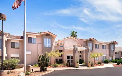 The hotel’s exterior has a fluttering USA flag flying from a flagpole and greenery including bushes, small trees, and a cactus.