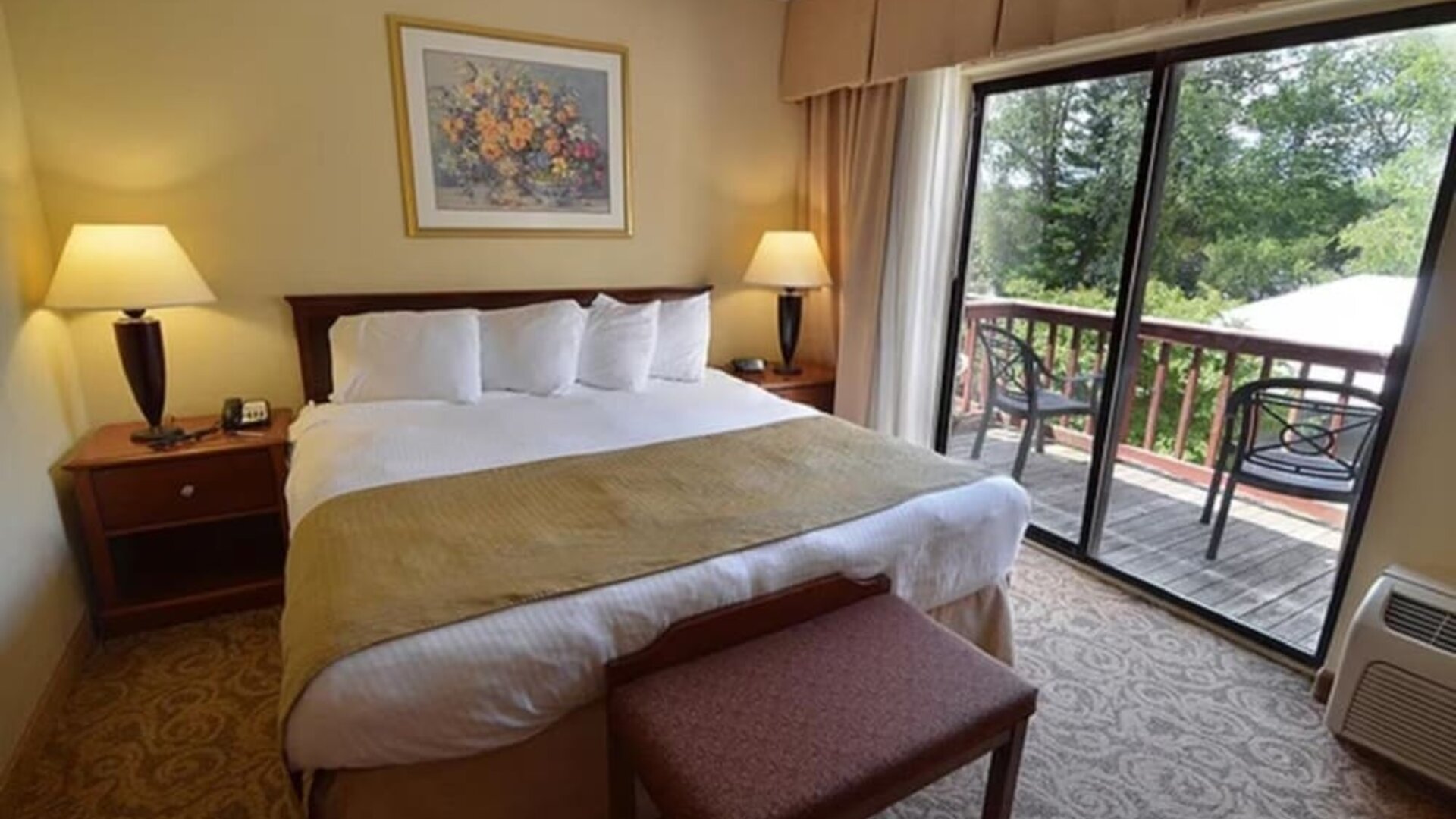 King guest room featuring plush bedding, private balcony access, and scenic outdoor views at Sturbridge Host Hotel.