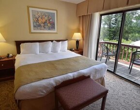 King guest room featuring plush bedding, private balcony access, and scenic outdoor views at Sturbridge Host Hotel.