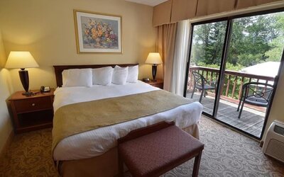 King guest room featuring plush bedding, private balcony access, and scenic outdoor views at Sturbridge Host Hotel.